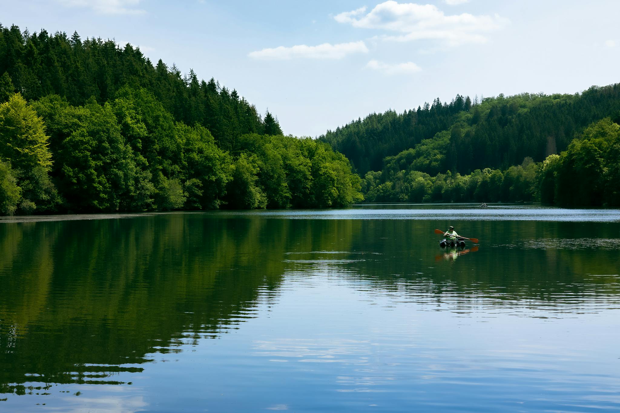 A lone kayaker enjoys a peaceful paddle on a scenic lake surrounded by lush greenery in Luxembourg.