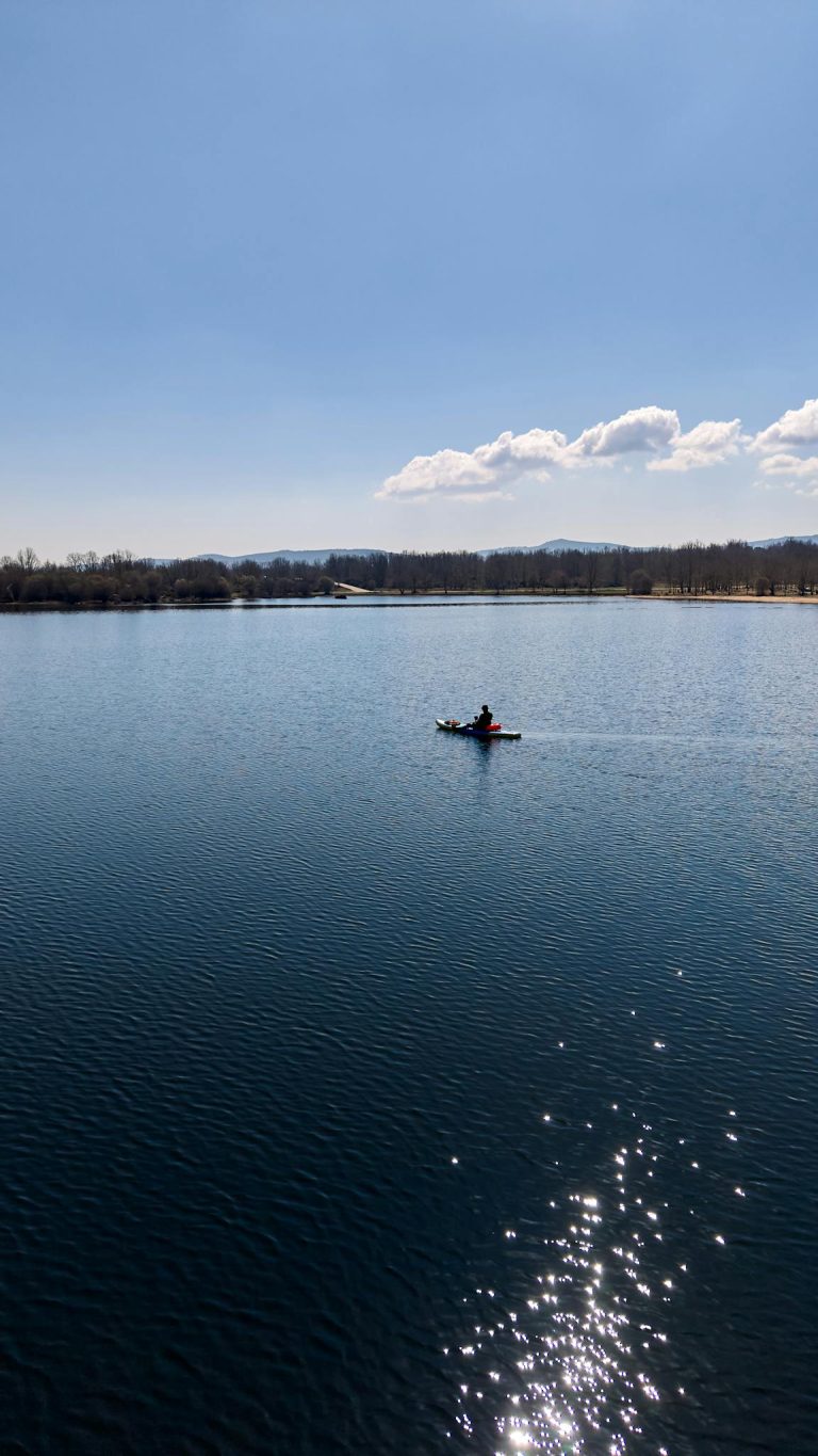A lone kayaker on a tranquil lake in Zamora, Spain, under blue skies.