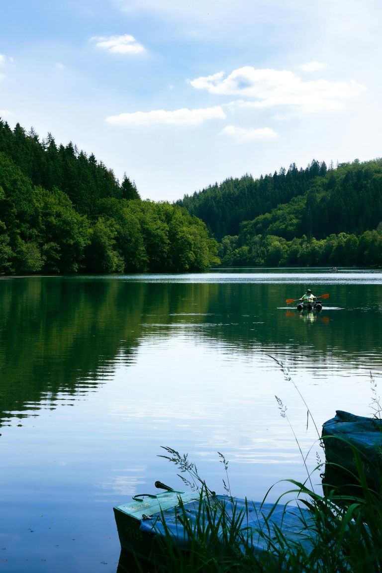 A tranquil scene of a person kayaking on a peaceful lake surrounded by lush forests in Luxembourg.