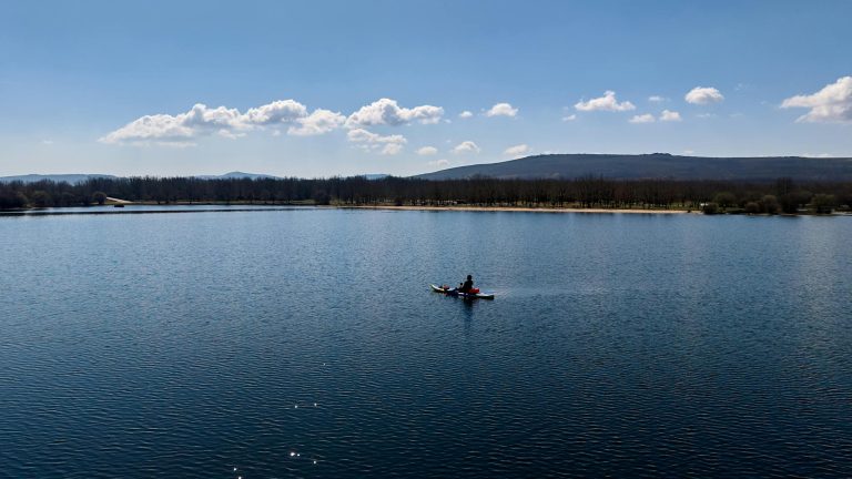 Serene view of a kayaker on a calm lake in Zamora under a clear blue sky.